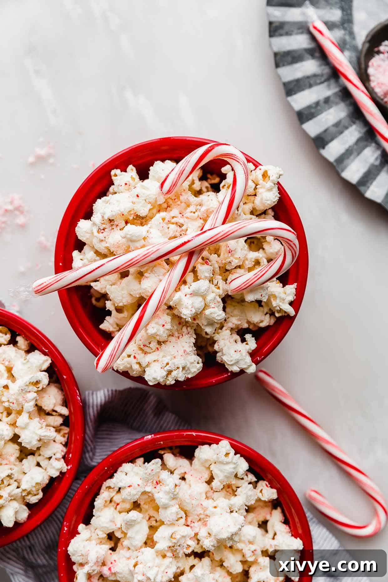 A vibrant red bowl overflowing with freshly made Candy Cane Popcorn, adorned with two whole candy canes on top, showcasing its festive appeal.