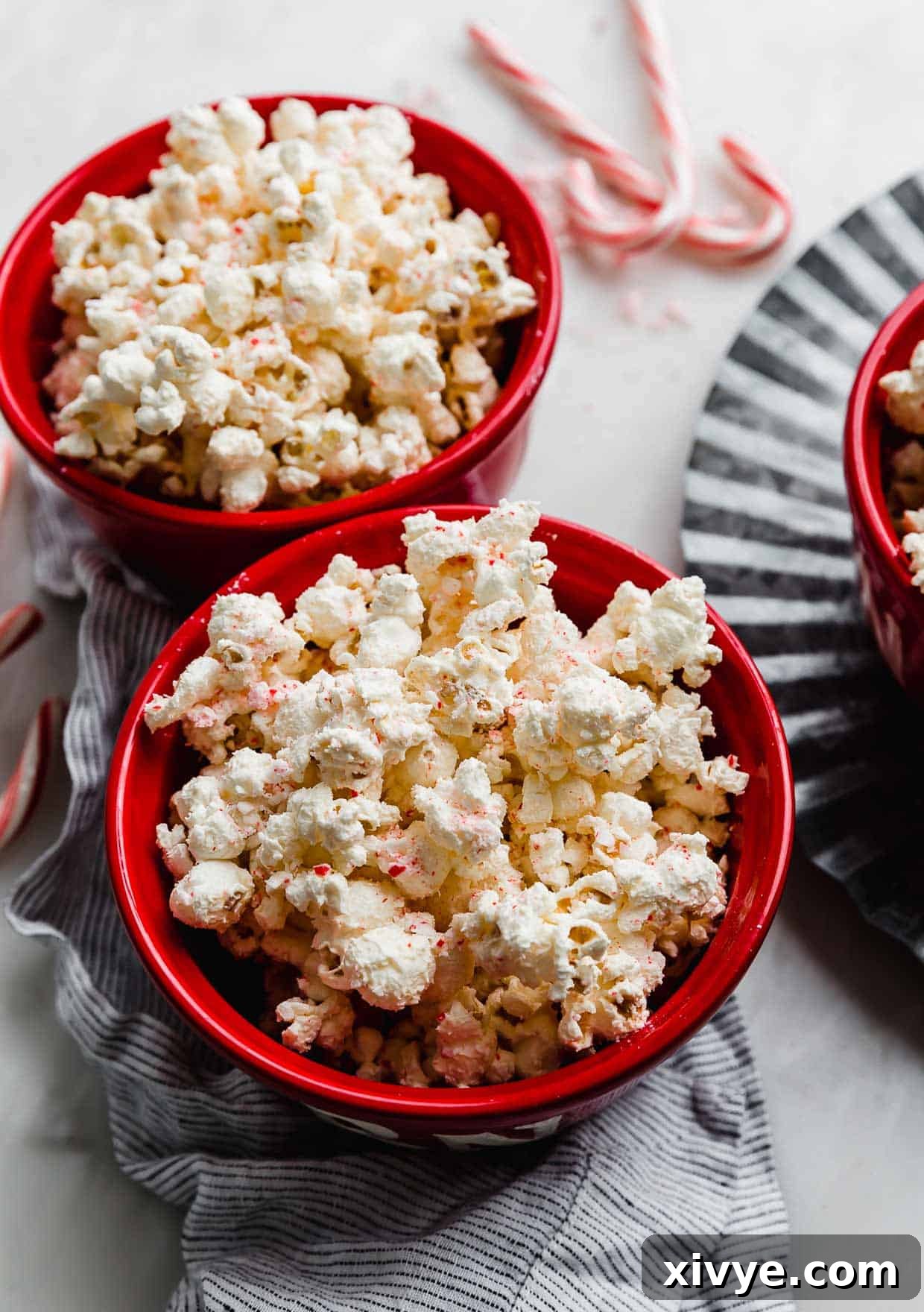 A charming red bowl filled to the brim with festive Candy Cane Popcorn, positioned against a soft, blurred background of more candy canes, evoking a warm holiday atmosphere.