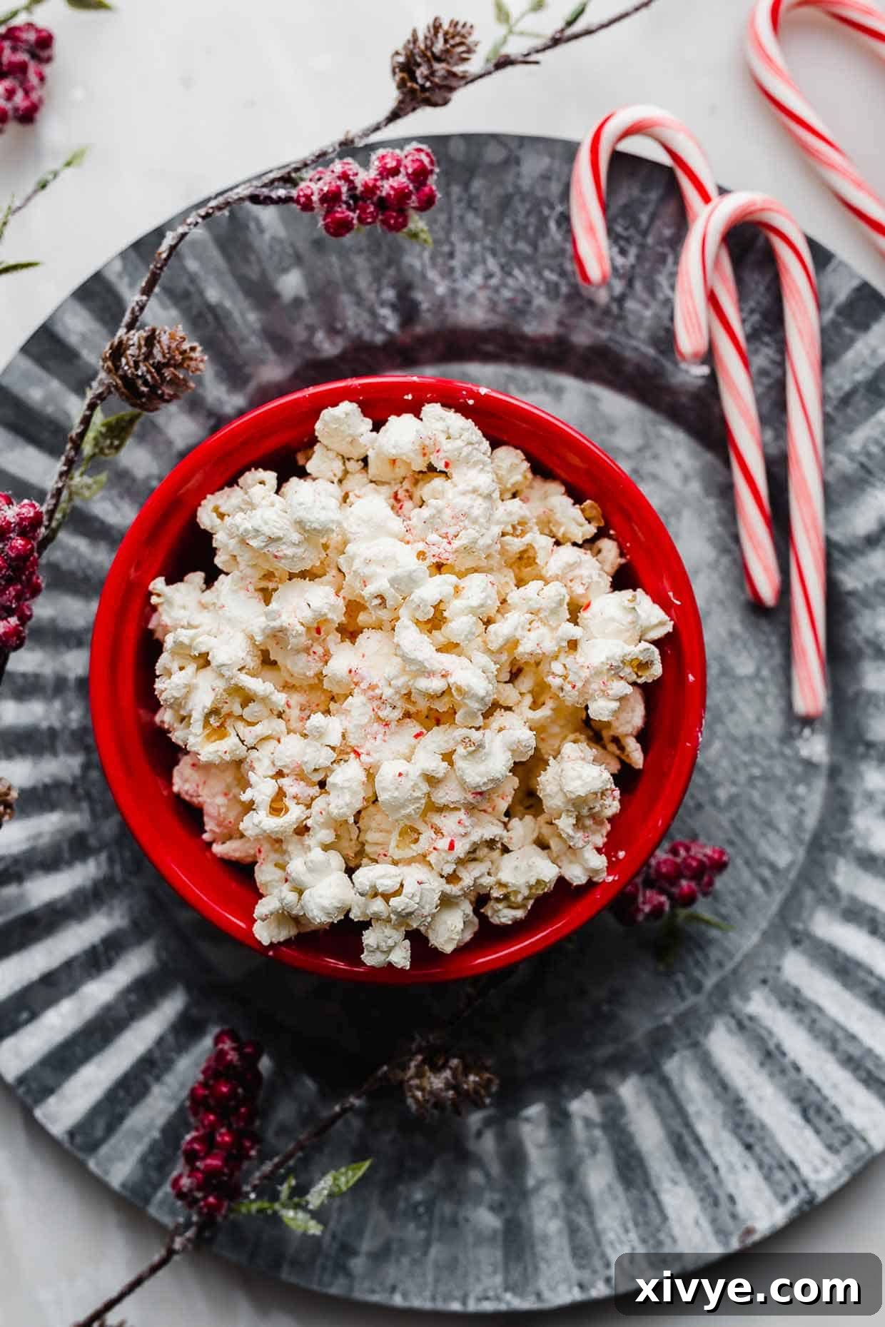A vibrant red bowl filled with glistening Candy Cane Popcorn, elegantly placed on a large, textured gray metal plate, ready for serving during the holidays.