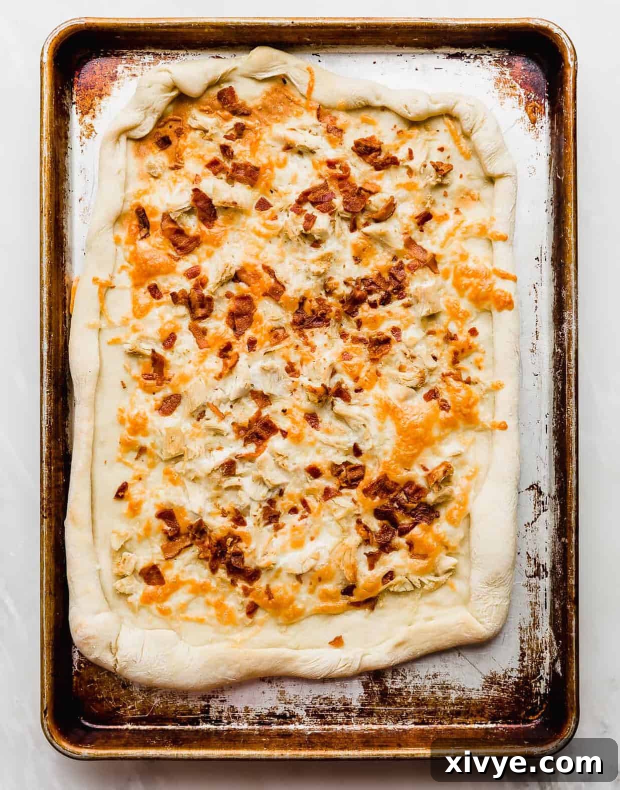 Baked pizza dough topped with cheese, bacon, and chicken.