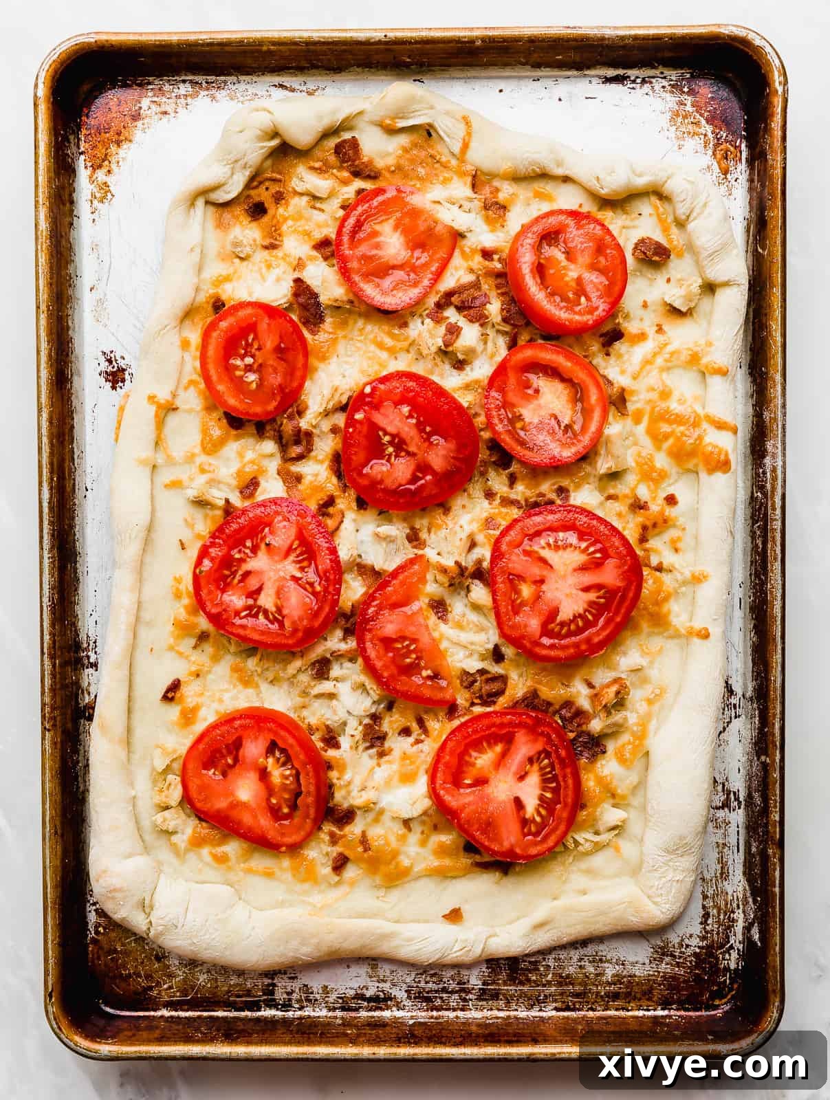 Tomato slices on top of a rectangular baked pizza dough. 