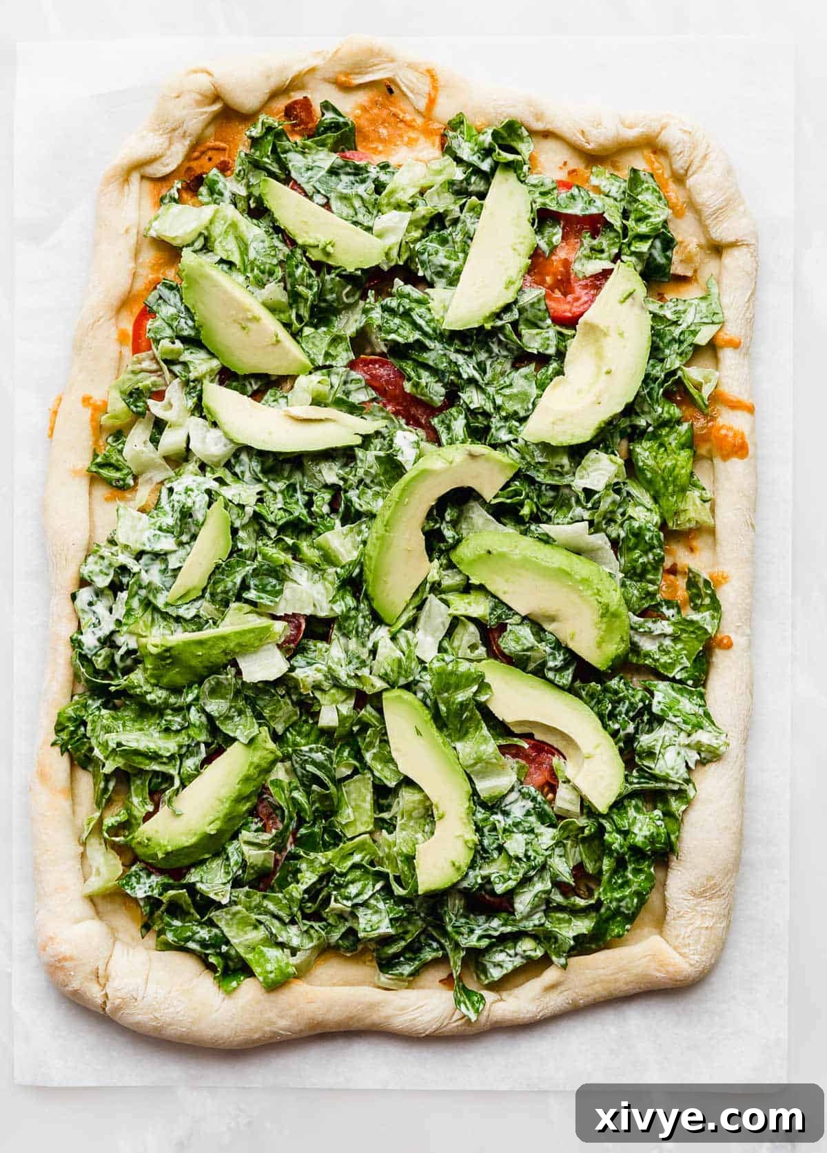 A rectangle type pizza topped with lettuce and avocado slices on a white background.