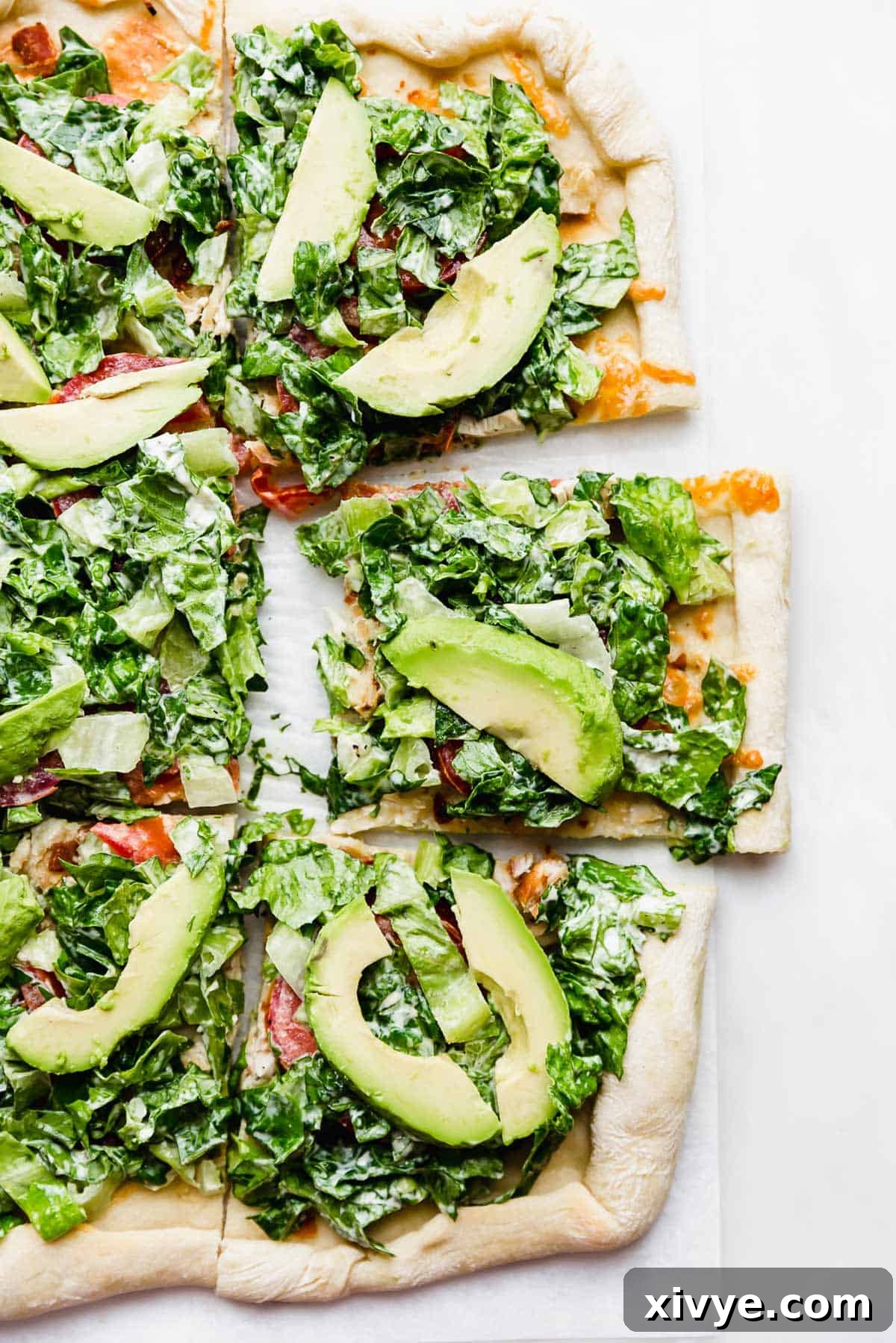 CPK Club Pizza topped with mayo covered lettuce, tomatoes, and avocado on a white background