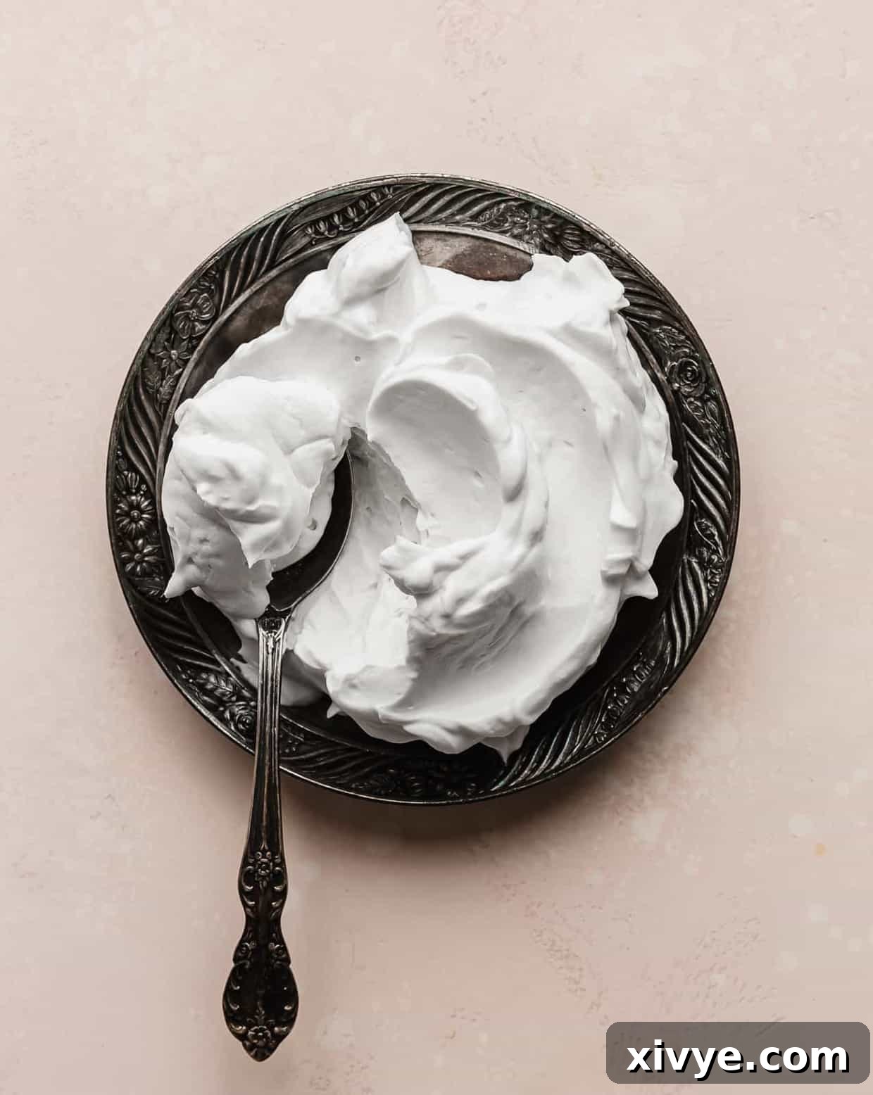 A plate full of pillowy Coconut Whipped Cream against a soft pink background.