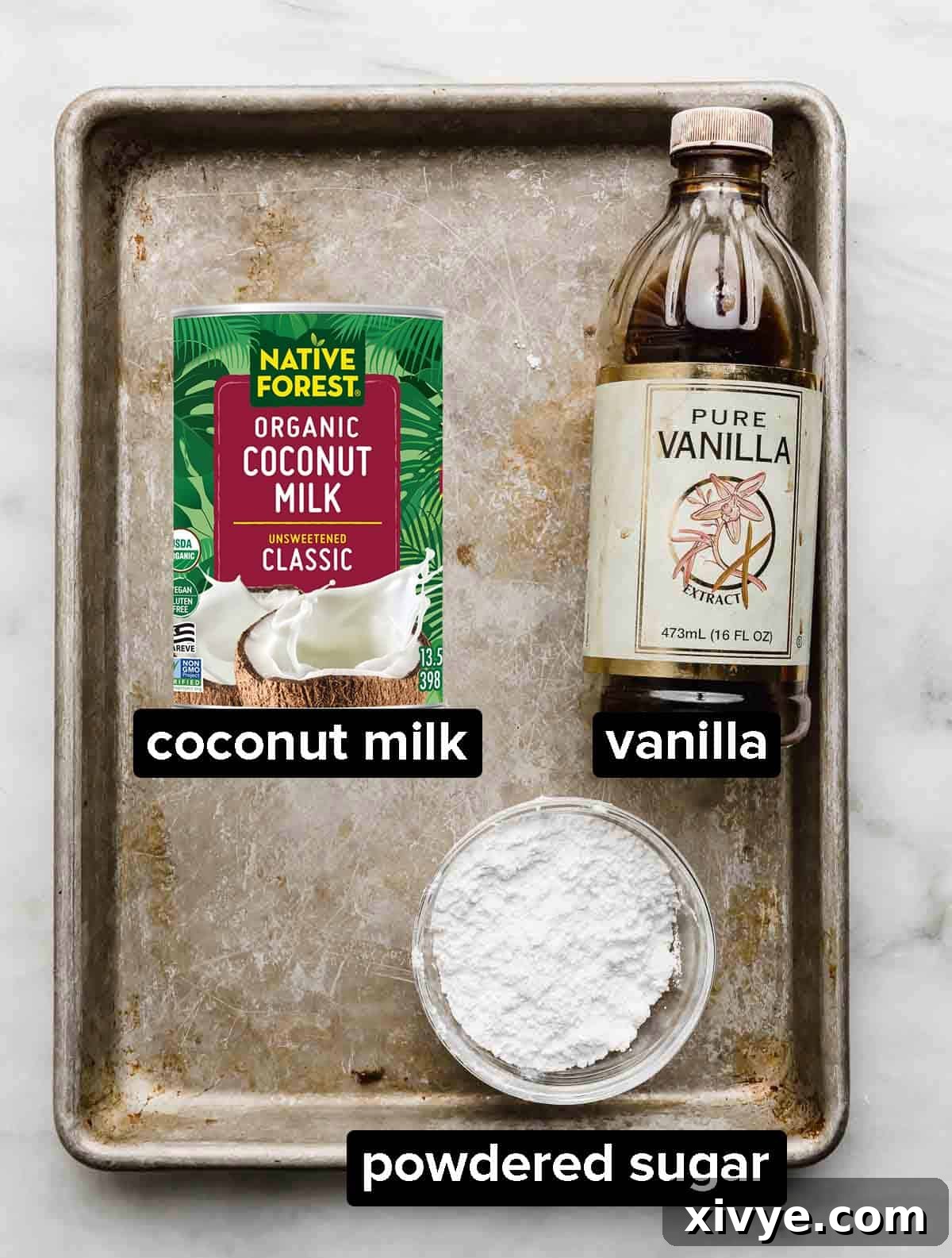 Ingredients used to make Coconut Whipped Cream on a silver baking sheet; canned coconut, vanilla, and powdered sugar.
