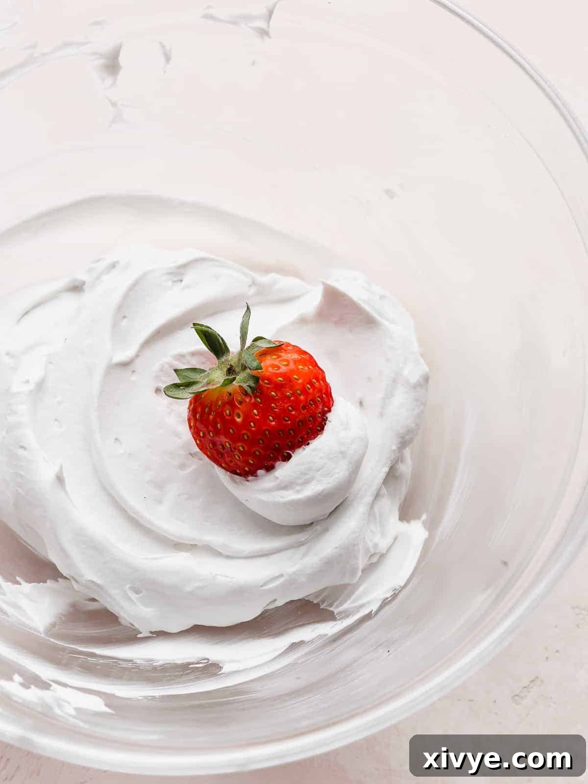 A red strawberry dipped into a pile of Coconut Whipped Cream.