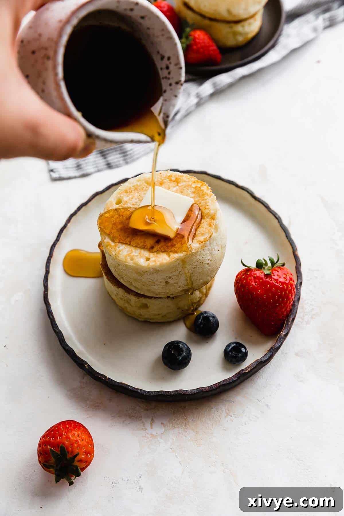 Japanese Soufflé Pancakes 8 Syrup pouring overtop two Fluffy Japanese Pancakes on a black rimmed white plate.