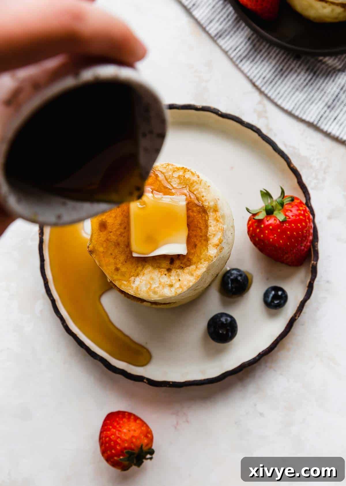 Japanese Soufflé Pancakes 9 Overhead photo of syrup being poured overtop Fluffy Japanese Pancakes on a black rimmed white plate.