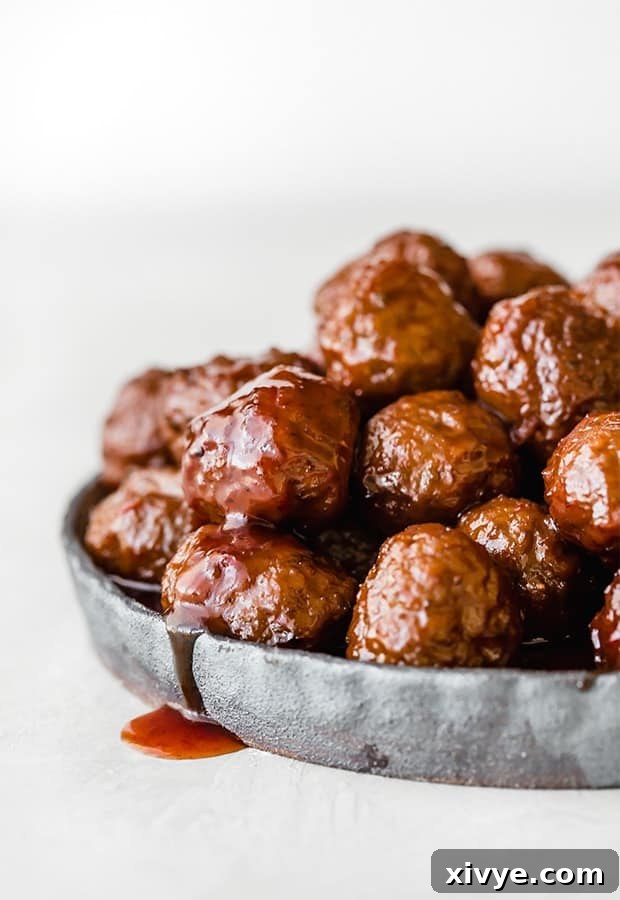 Strategic Eating: Week 2 5 Grape jelly meatballs on a black rimmed plate with sauce drizzling over the side of the plate, looking enticing.