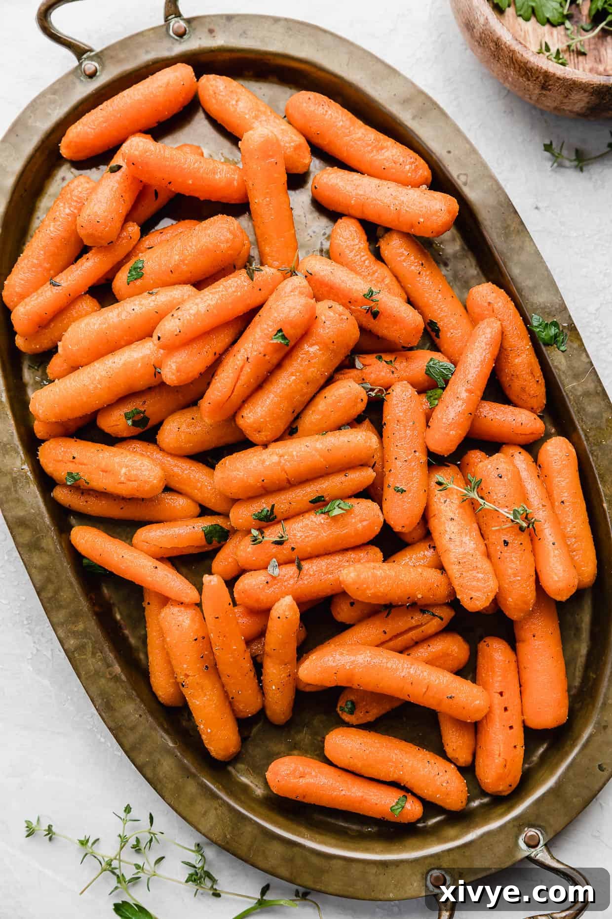 Roasted Baby Carrots topped with thyme and parsley on a bronze oval plate.