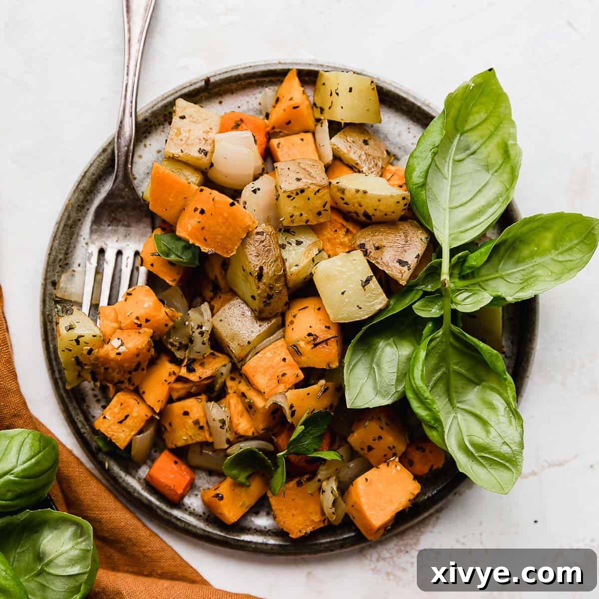 A gray plate on a white background with easy Sheet Pan Roasted Root Vegetables topped with herbs on it.