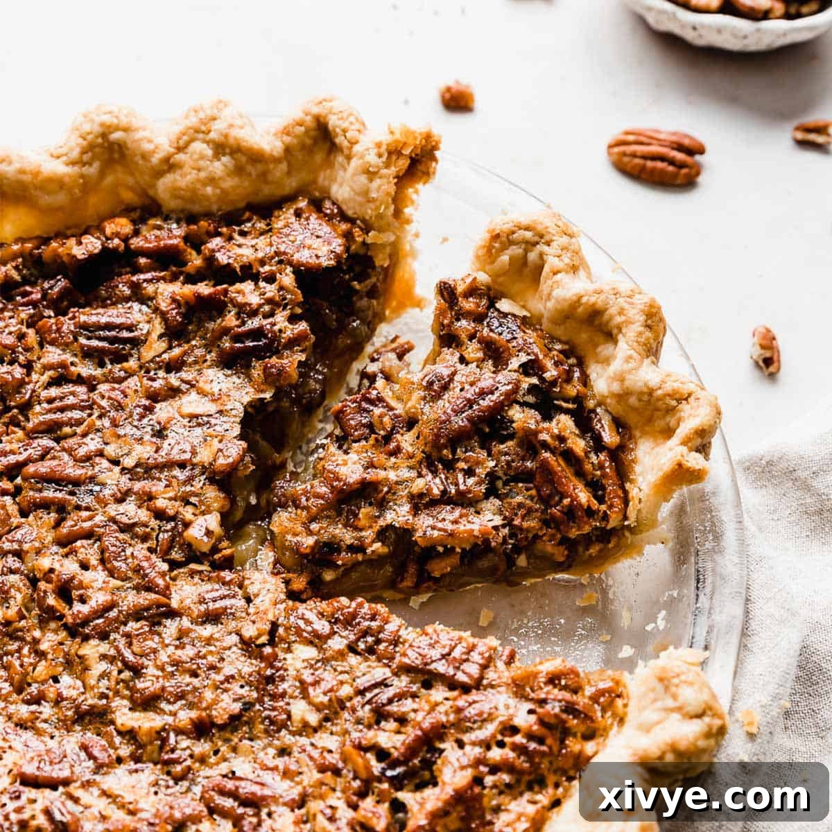 A pecan pie on a white background with pecan pieces in the background.