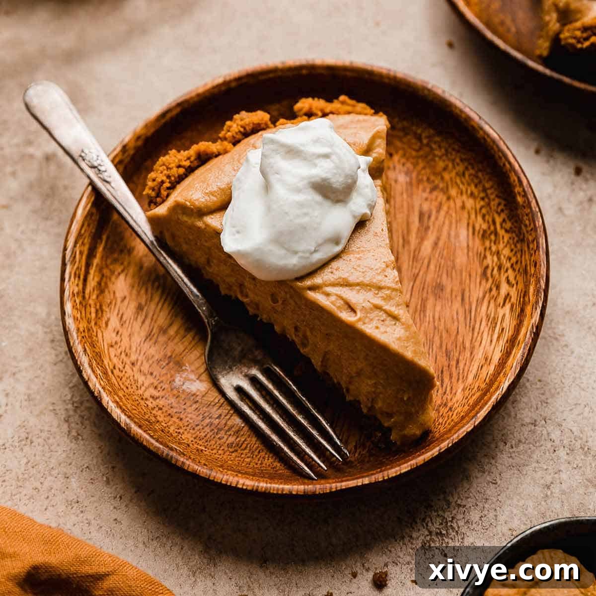 Biscoff Pumpkin Pie topped with whipped cream on a wood plate.