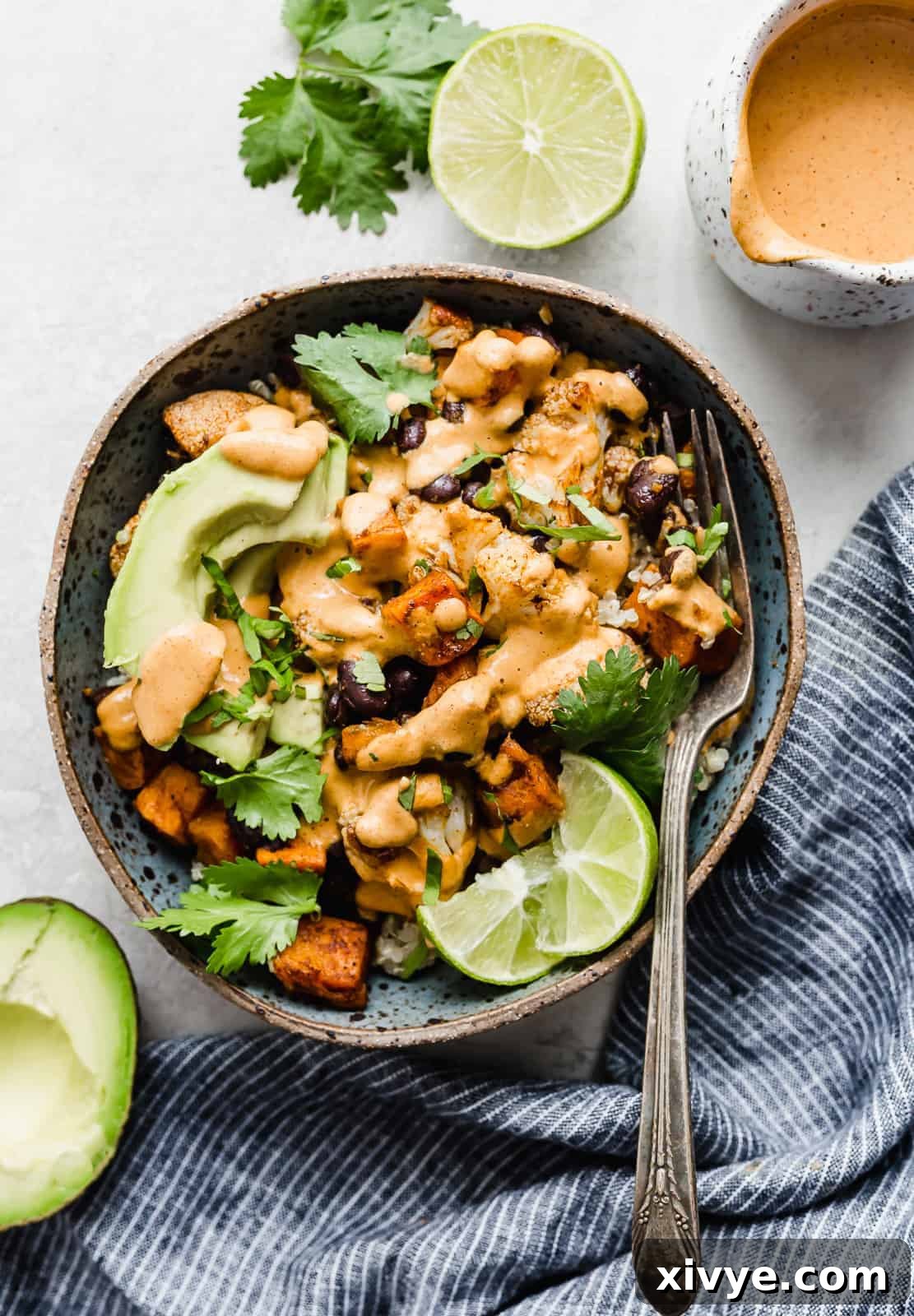 A beautifully composed blue bowl brimming with fluffy quinoa, generously topped with perfectly roasted sweet potatoes and tender cauliflower florets, inviting a delightful meal.
