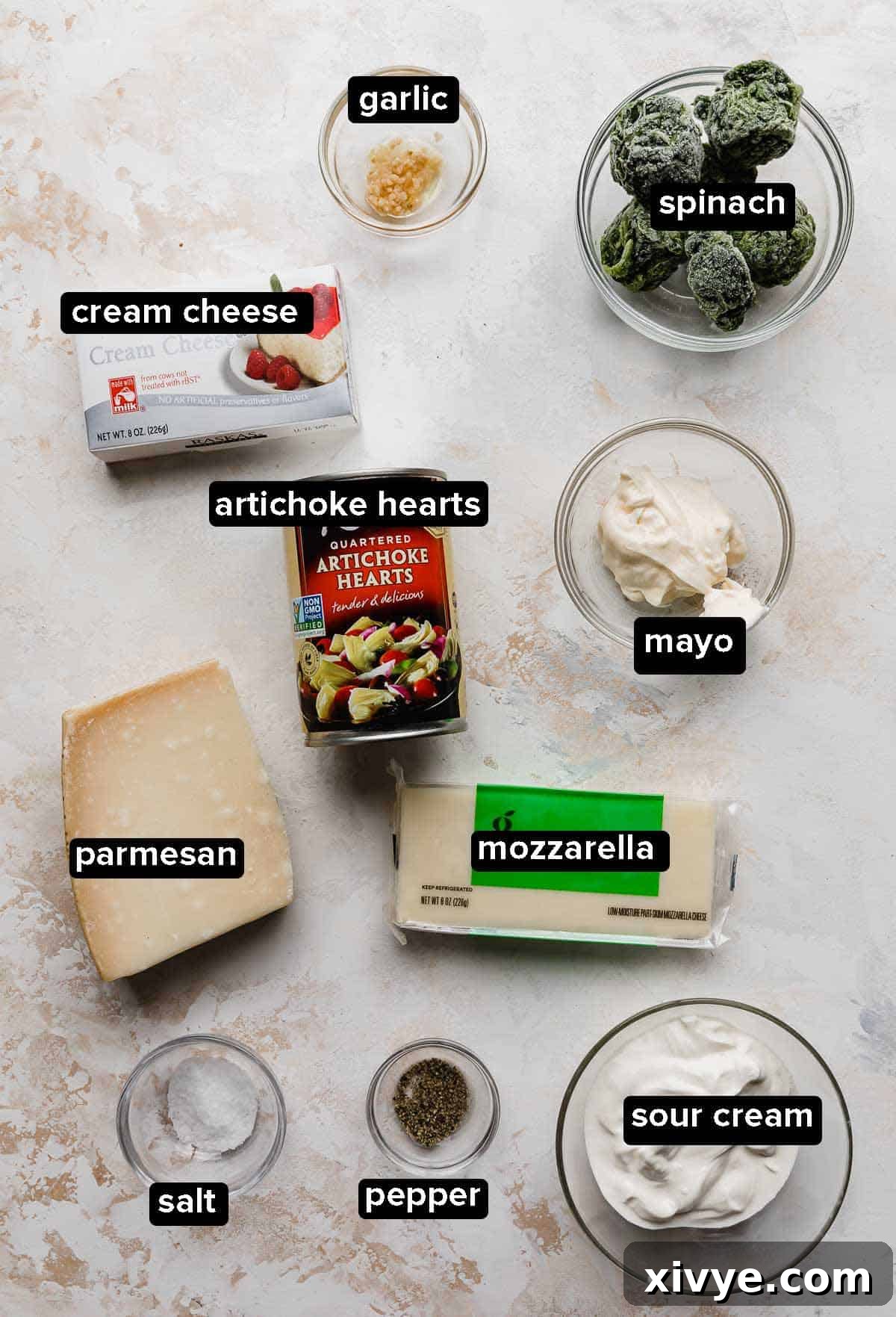 Sizzling Spinach Artichoke Delight 3 All the fresh ingredients for Hot Spinach Artichoke Dip, including cheeses, sour cream, mayo, spinach, and artichokes, beautifully arranged on a white and cream textured background.