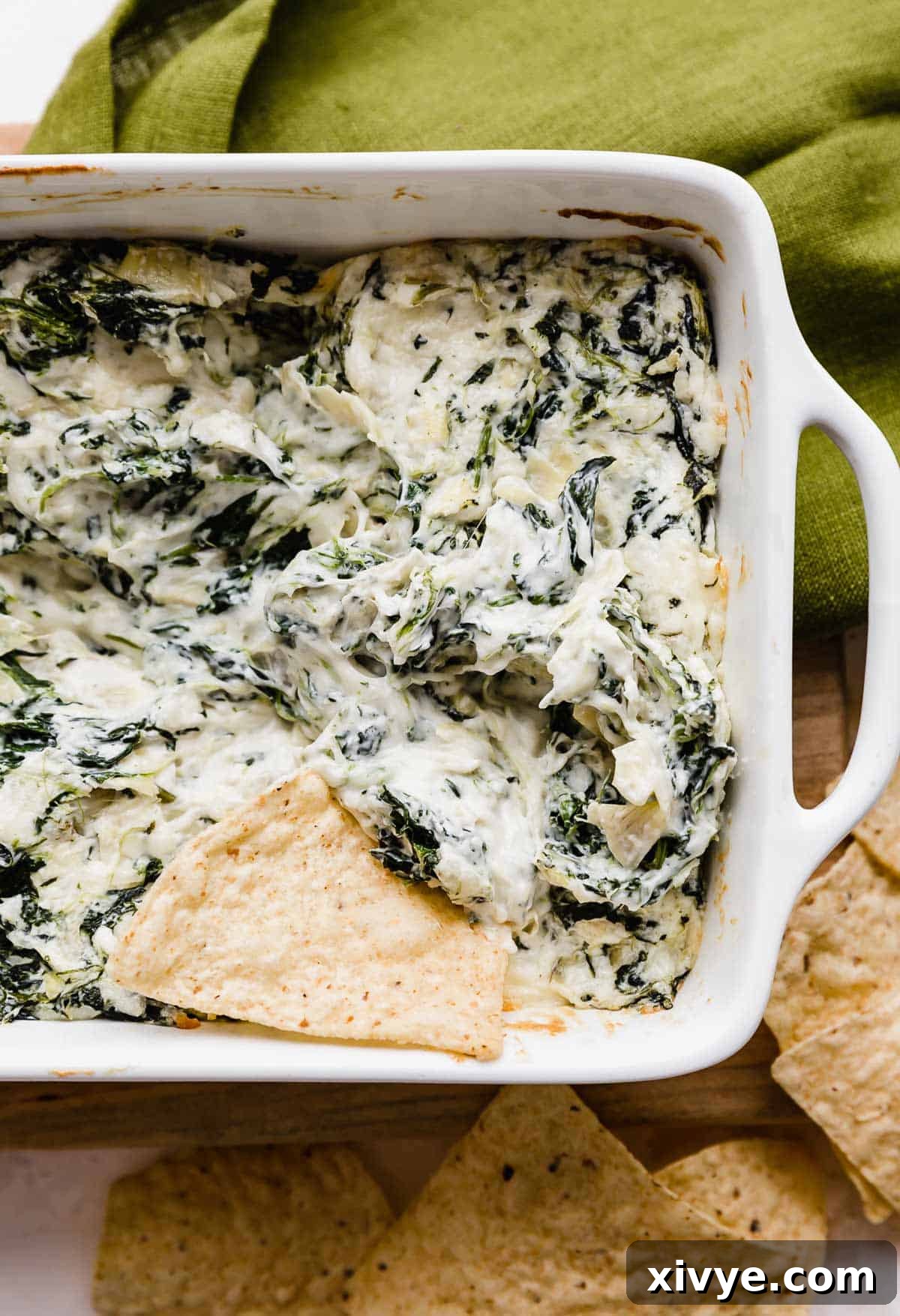 Sizzling Spinach Artichoke Delight 5 A single tortilla chip positioned perfectly to scoop into a hot, bubbly pan of Spinach Artichoke Dip, inviting guests to enjoy.