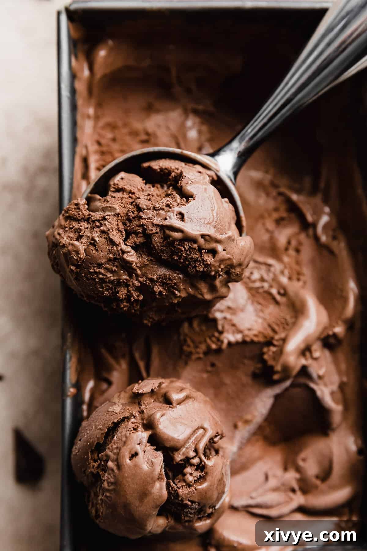 An ice cream scooper efficiently scooping out rich dark chocolate ice cream from a rectangle container, highlighting its dense and intensely dark appearance.