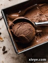 The best dark chocolate ice cream in a bread pan with an ice cream scooper scooping out a ball of the brown ice cream, ready to serve.