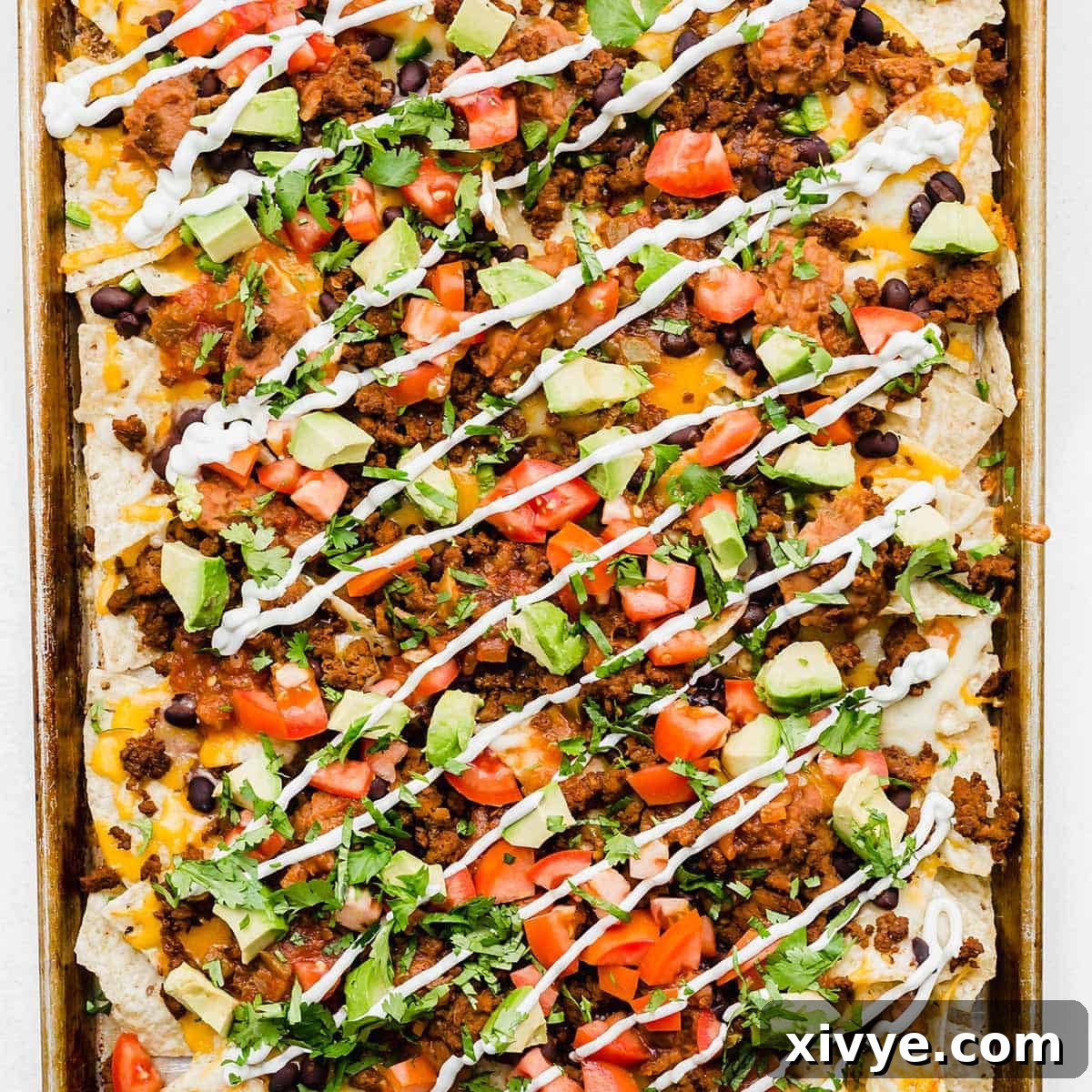 Sheet pan nachos topped with beef, sour cream, tomatoes, cilantro, and avocado.