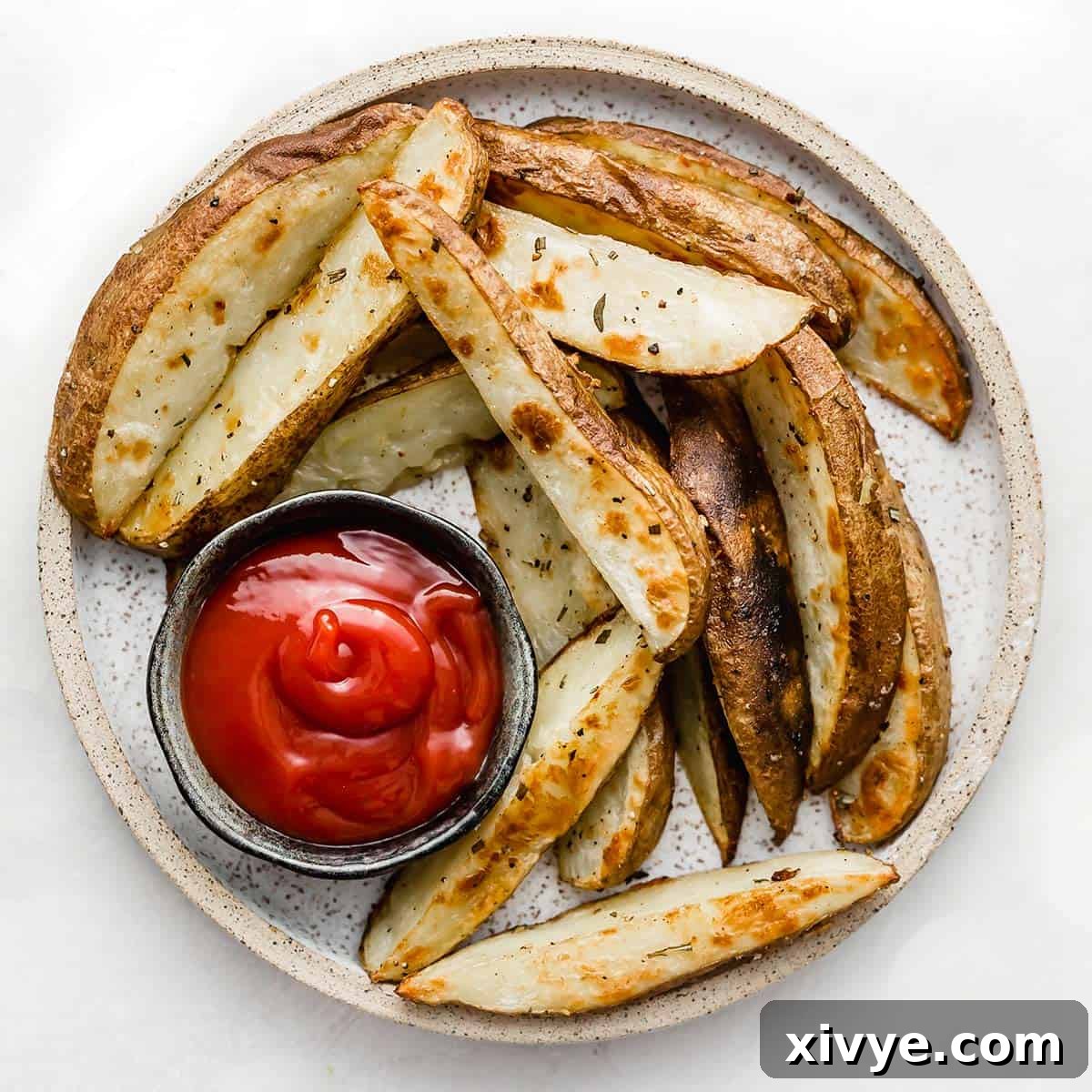 A round white plate with Crispy Baked Potato Wedges on it with a bowl of ketchup, on a white background.