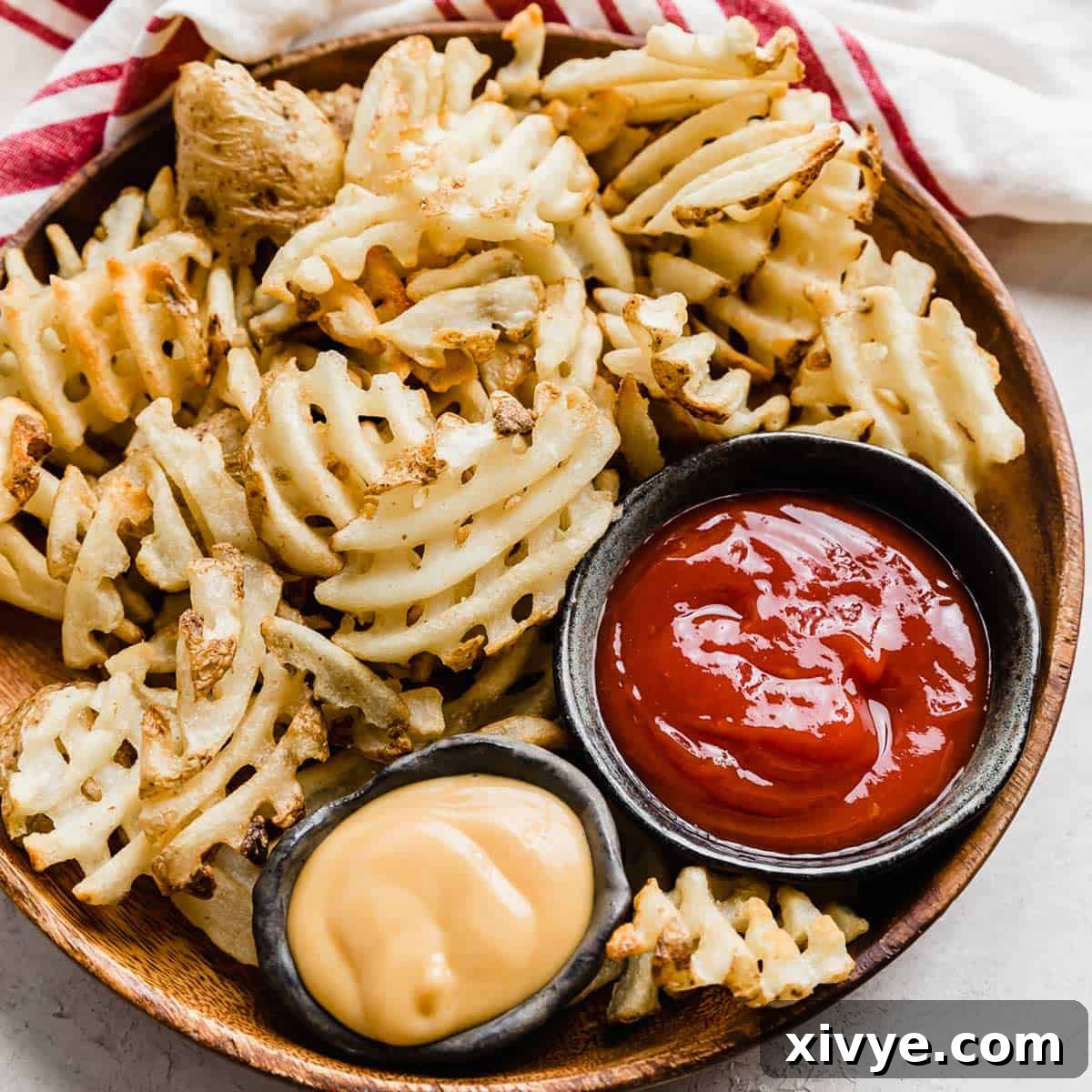 Waffle fries on a brown plate with bowls of ketchup and chick fil a sauce beside them.