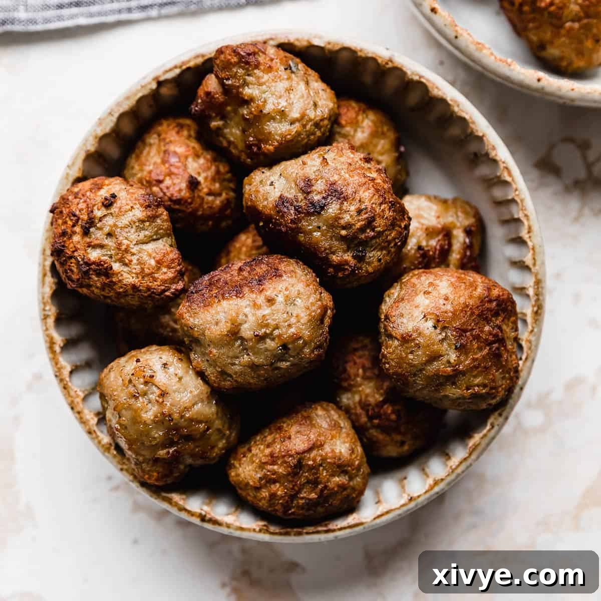 Meatballs cooked in the air fryer in a ceramic bowl on a white background.