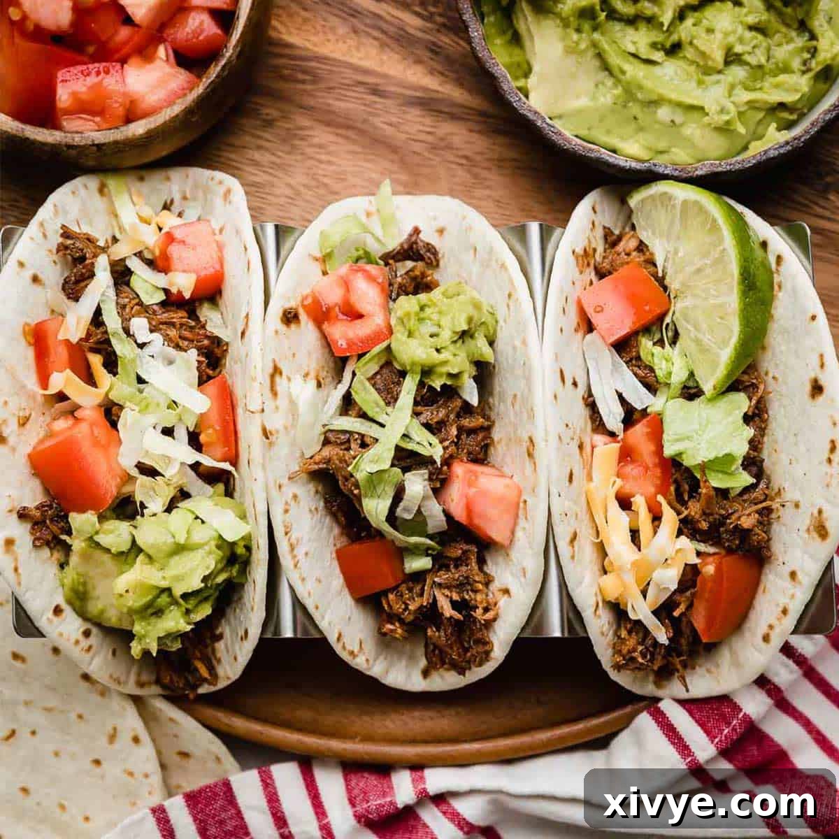Three flour tortillas filled with Crock Pot Shredded Beef Taco mix, shredded lettuce, guacamole, and tomatoes.