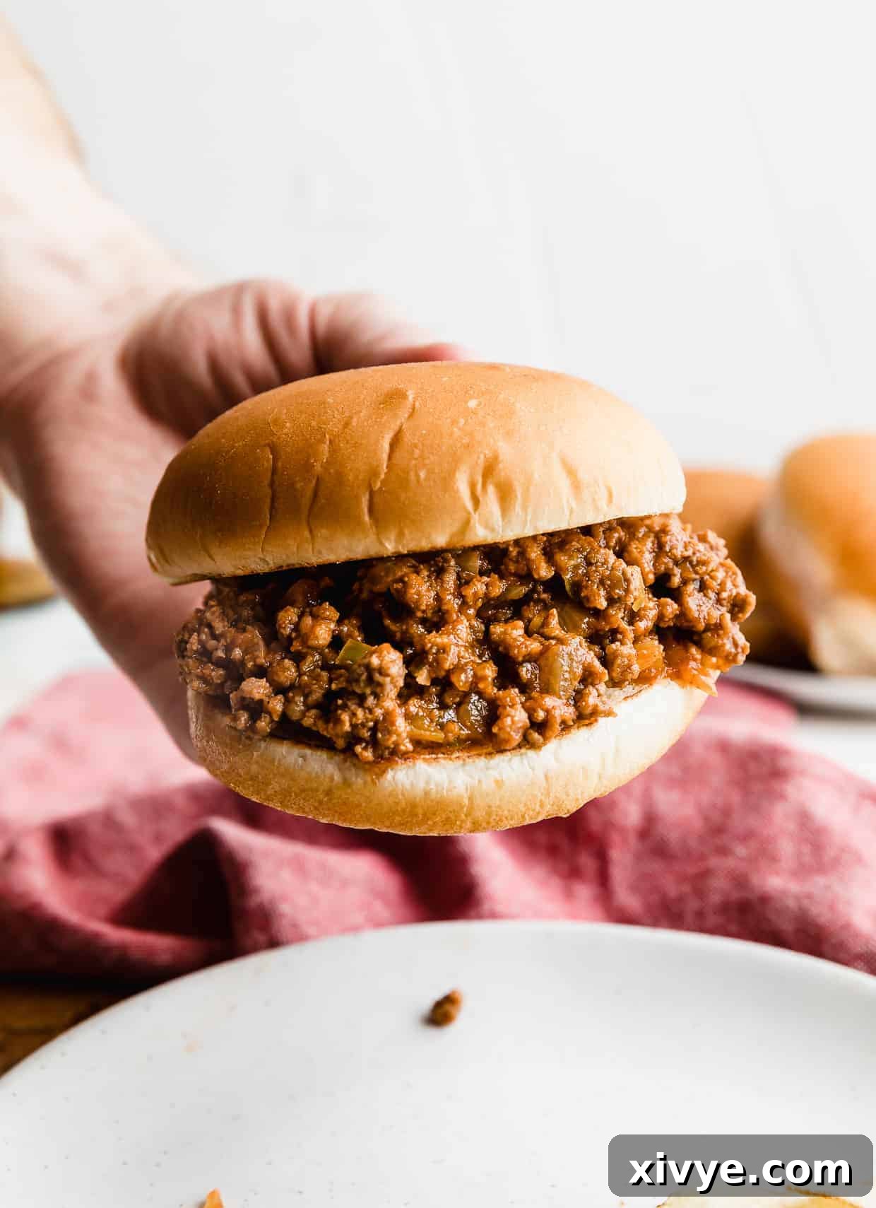 A hand holding up a hamburger bun that is very full of the best homemade sloppy Joe mix.