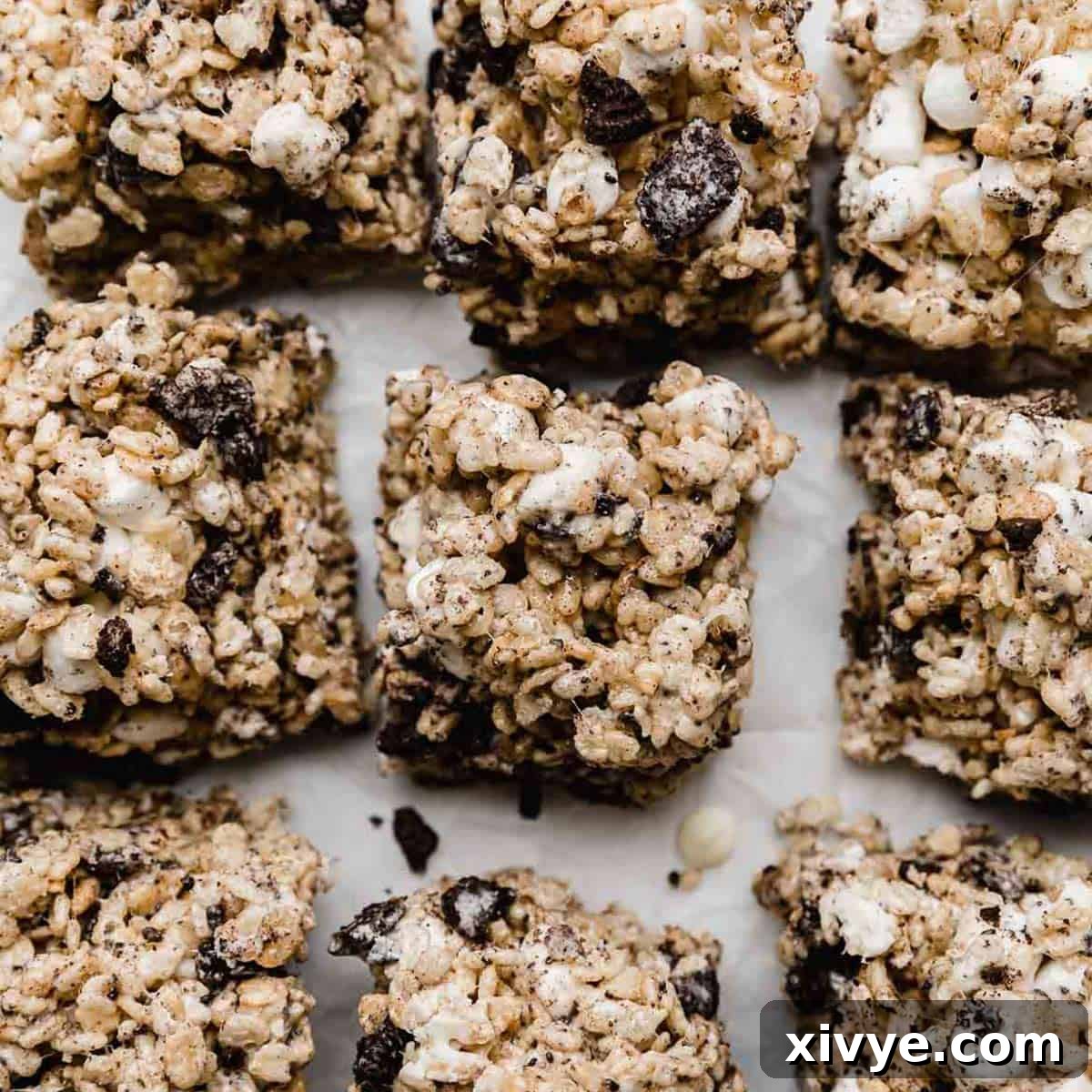 Cookies and Cream Rice Krispies treats with chopped Oreos in it, cut into squares on a white surface.