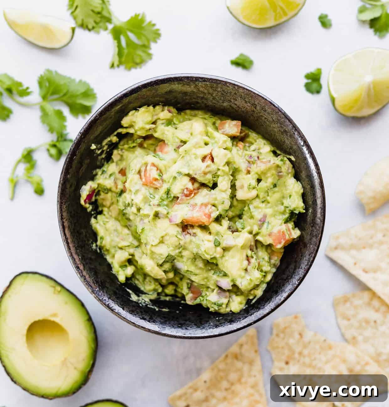 Bowl of guacamole surrounded by tortilla chips, cilantro, and limes.