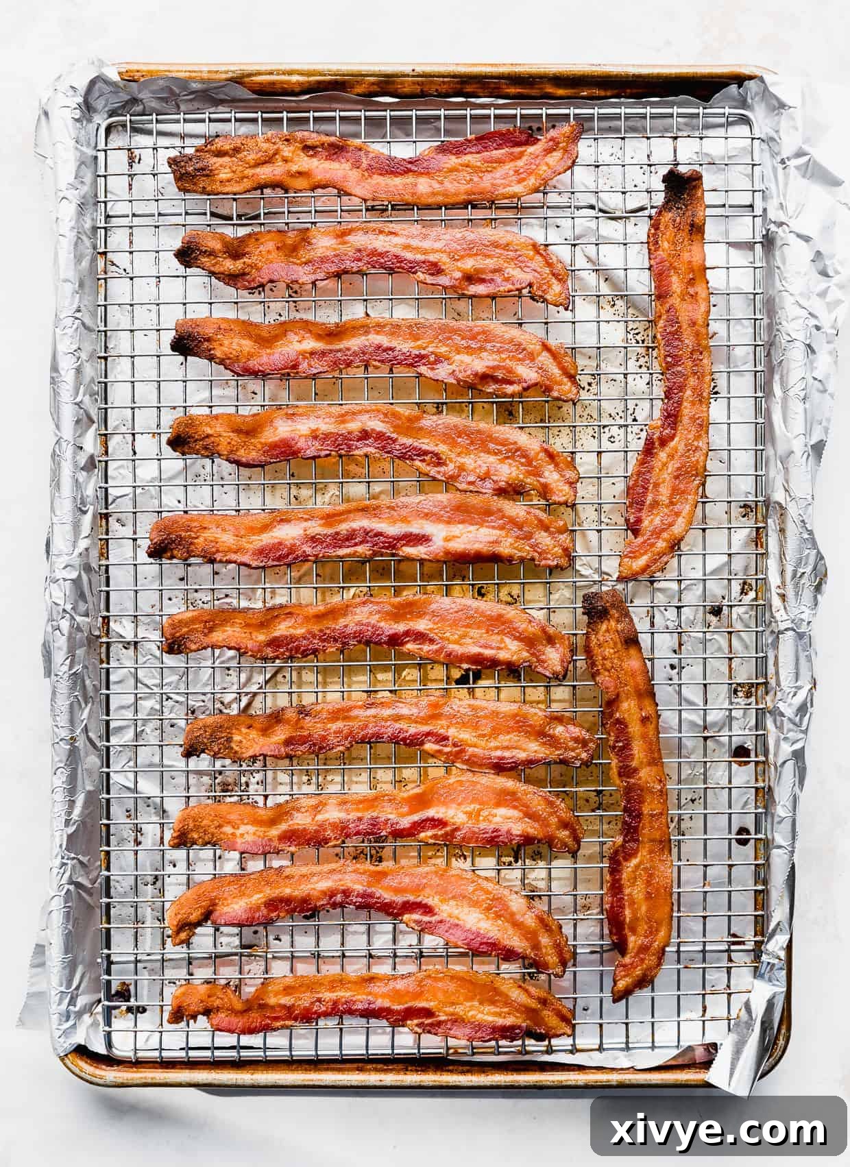 The Secret to Perfectly Crispy Oven Bacon 5 Freshly baked, perfectly crispy bacon strips on a wire rack, just removed from the oven and glistening with deliciousness.