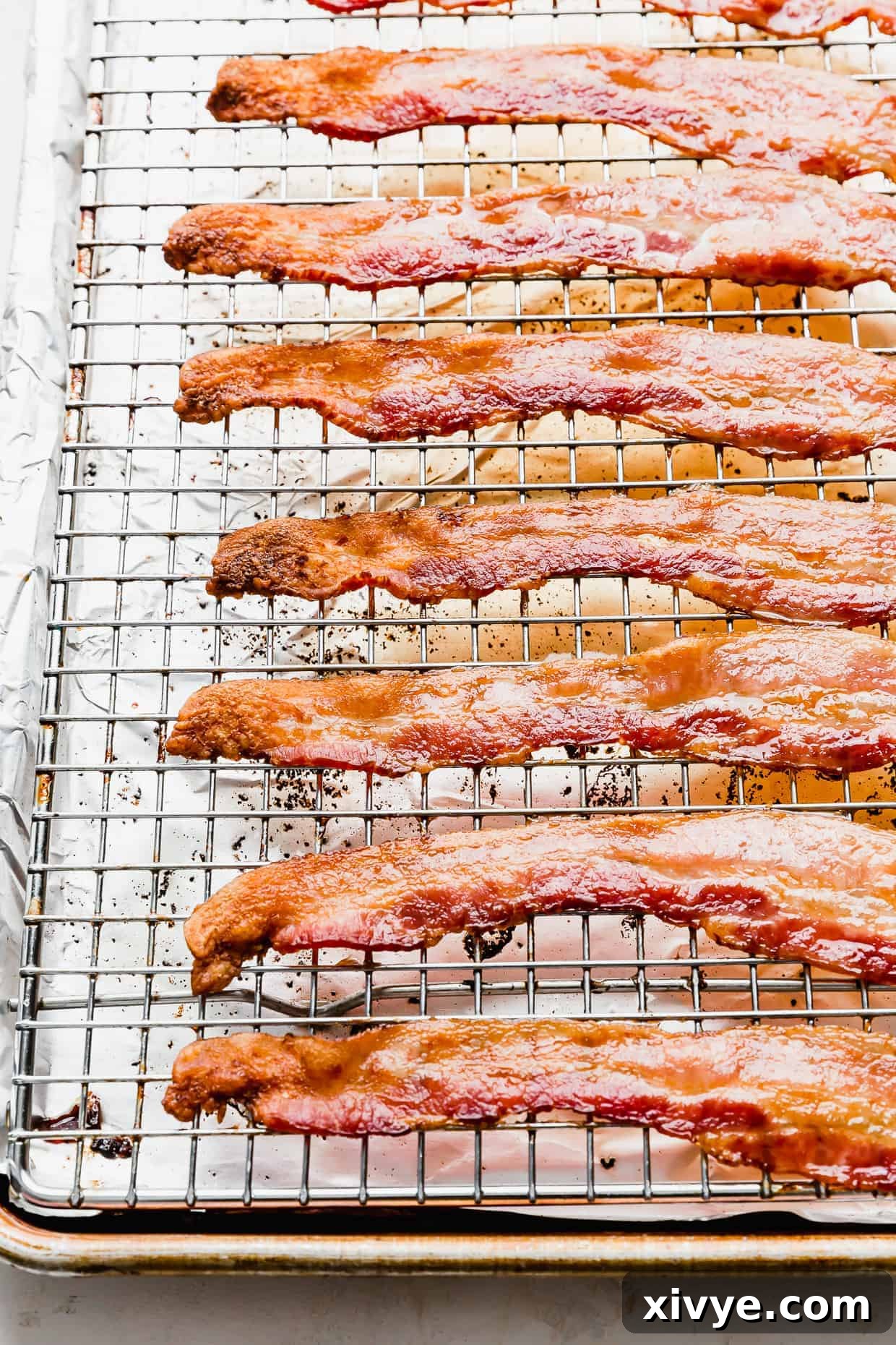 The Secret to Perfectly Crispy Oven Bacon 6 An appetizing angled shot of golden-crisp bacon resting on a wire rack within a baking sheet, glistening and ready to be enjoyed.