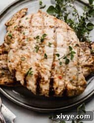 Italian Grilled Chicken surrounded by fresh herbs, on a gray plate.