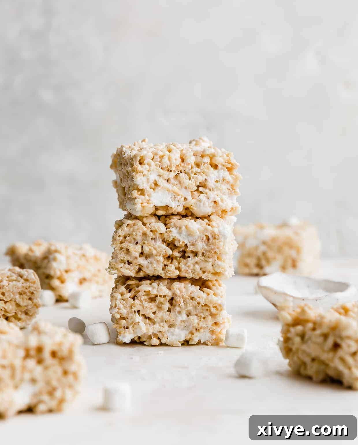 Three, thick, brown butter Rice Krispie treats stacked on top of each other, with mini marshmallows scattered around the base.