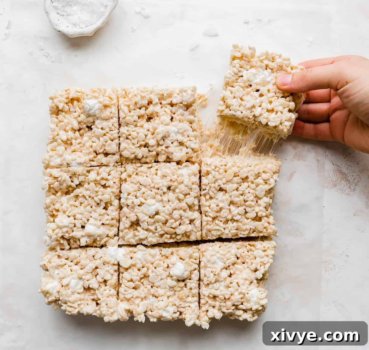 A hand grabbing a cut square of Salted Brown Butter Rice Krispie Treats.
