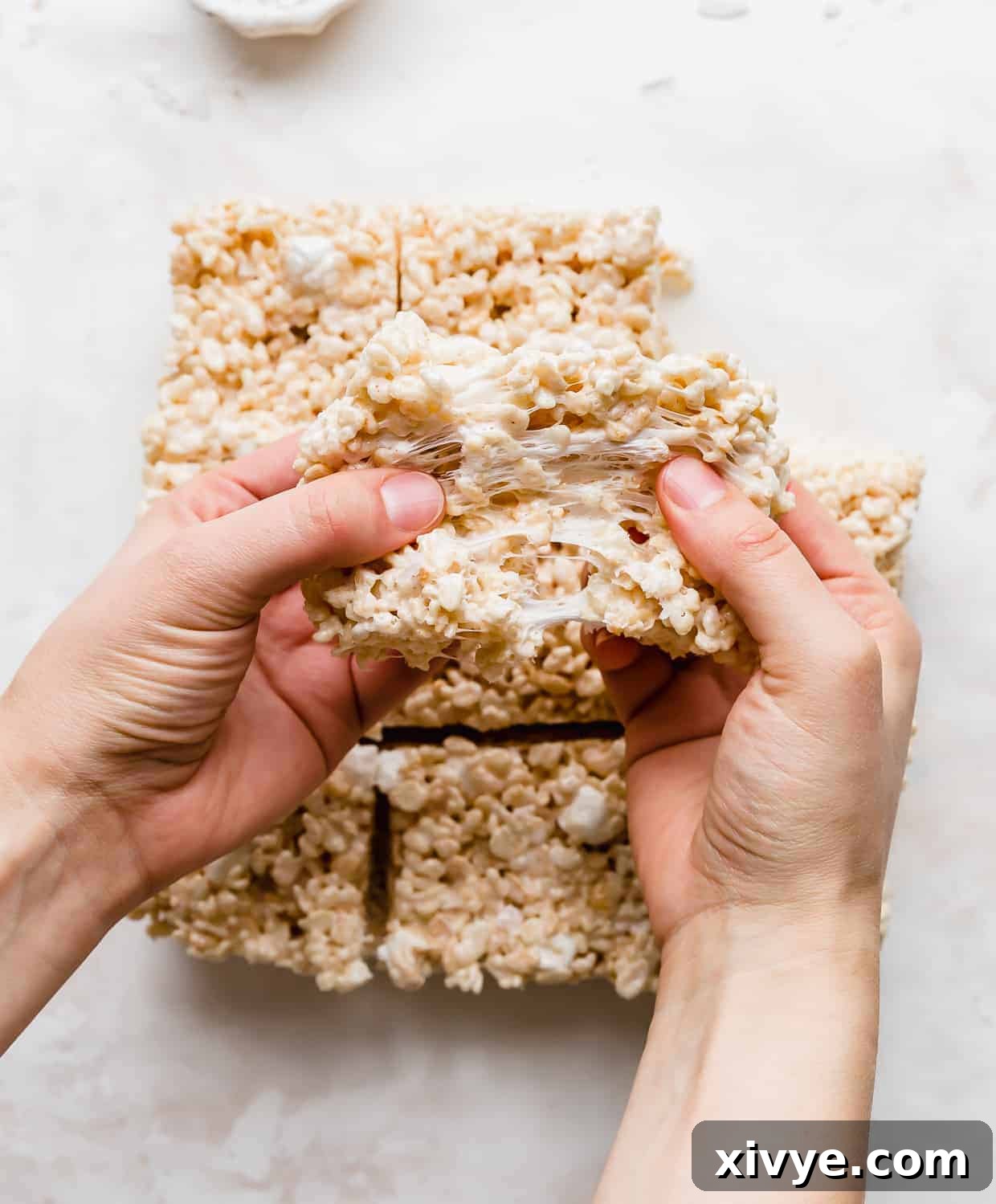 A pair of hands pulling a gooey Rice Krispie treat apart. 