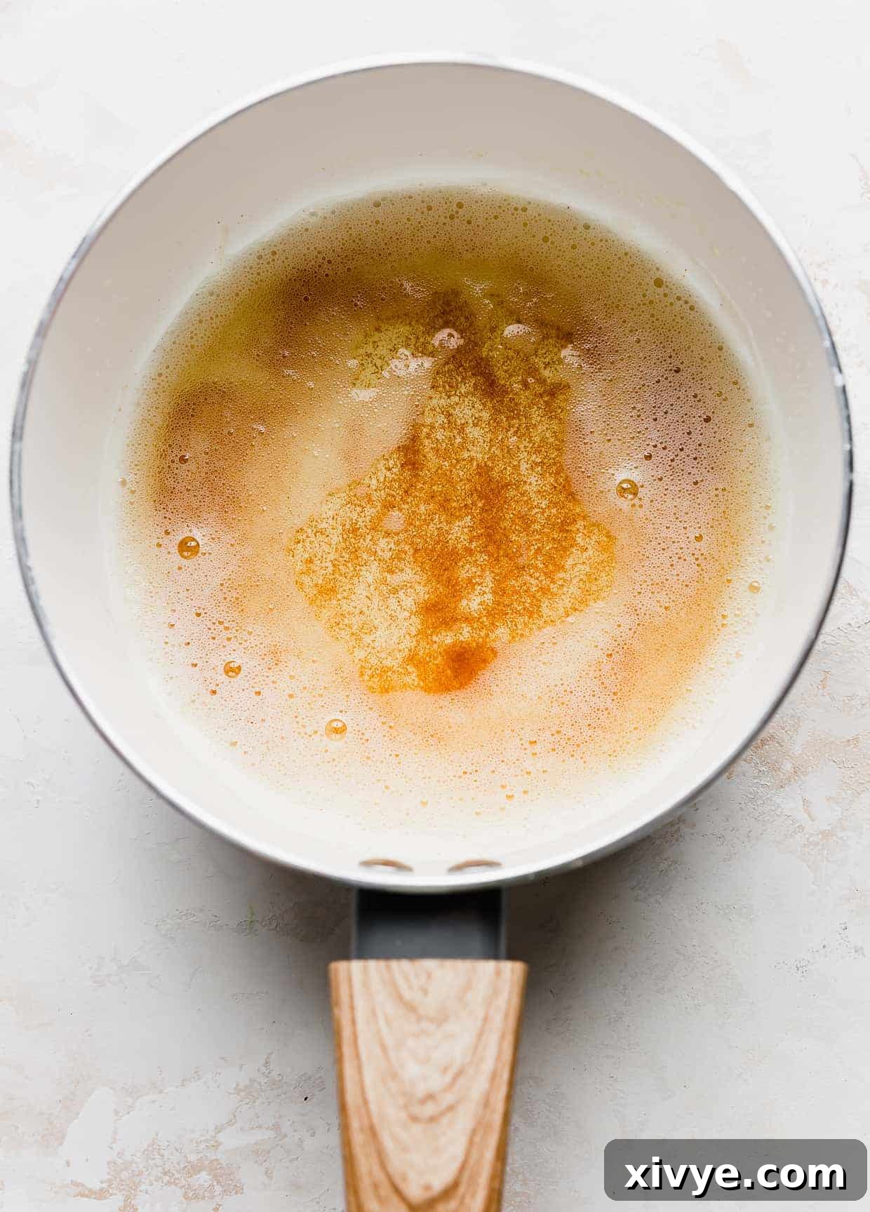 A white sauce pan with browned butter (a light amber color) in it.