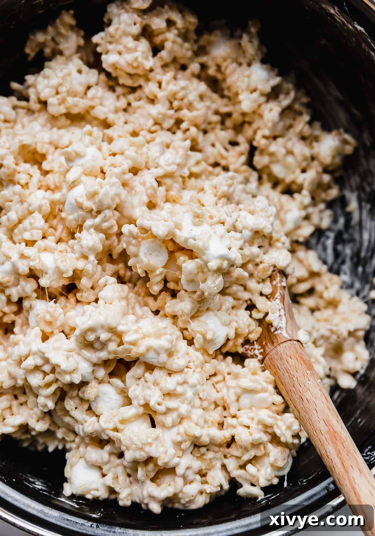 A close up photo of Rice Krispie treats being stirred in a pot with a wooden spoon.