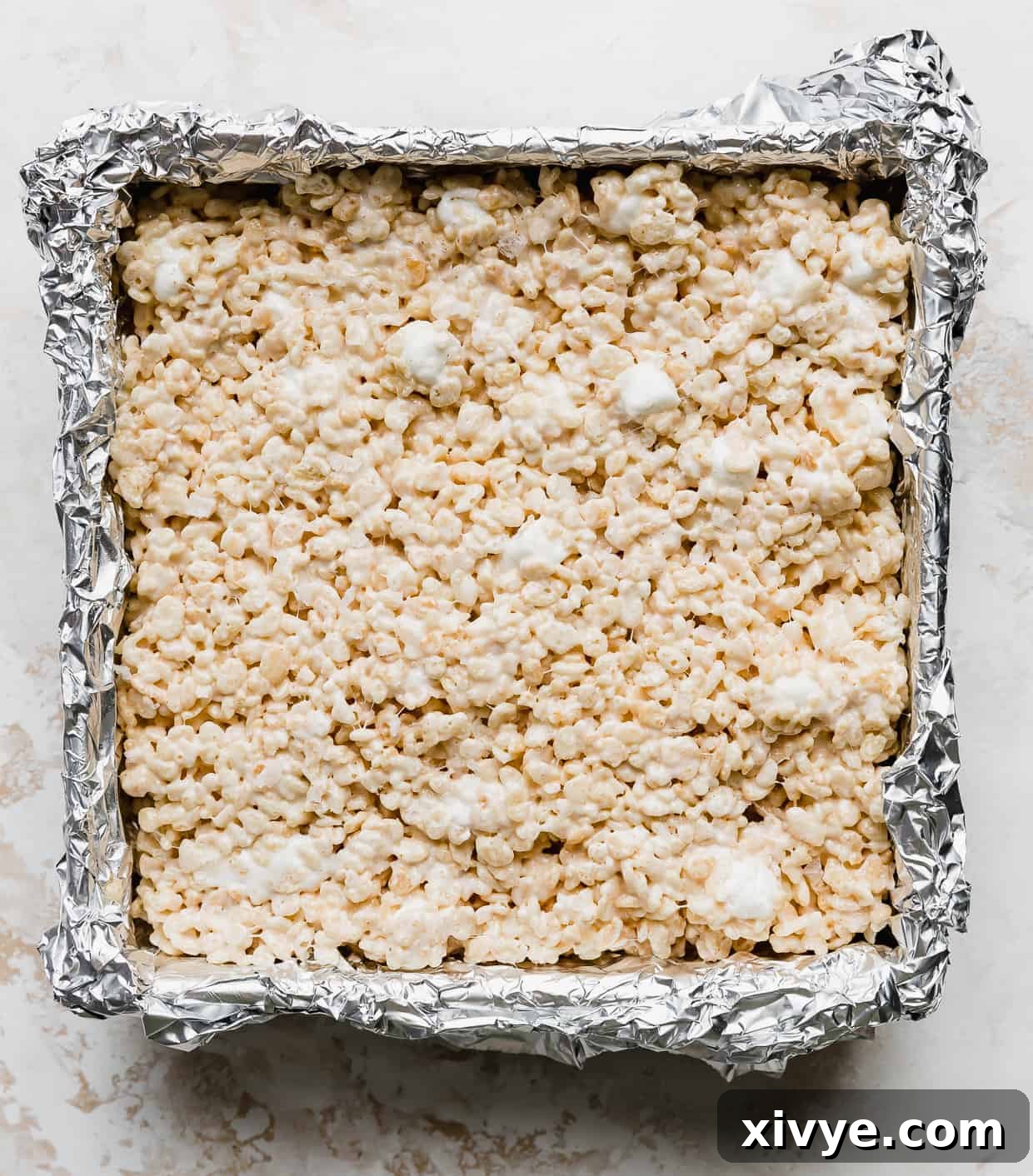 Salted Brown Butter Rice Krispie Treats pressed into a foil lined square pan against a white background.