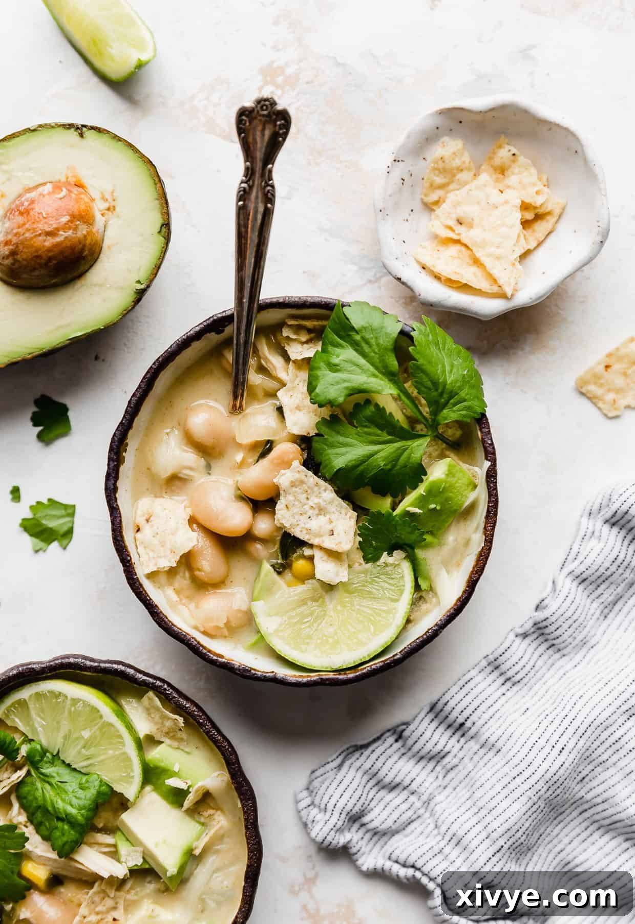 Creamy White Chicken Chili 2 A beautiful bowl of white chicken chili, garnished with fresh cilantro, a lime wedge, and crispy crushed tortilla chips, ready to be enjoyed.