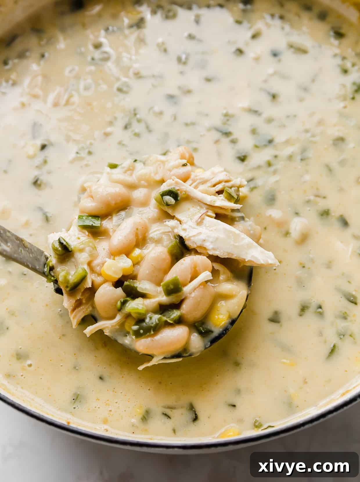 Creamy White Chicken Chili 6 A ladle gracefully scooping up a portion of the rich and creamy Best White Chicken Chili from a large pot, showcasing its hearty texture.