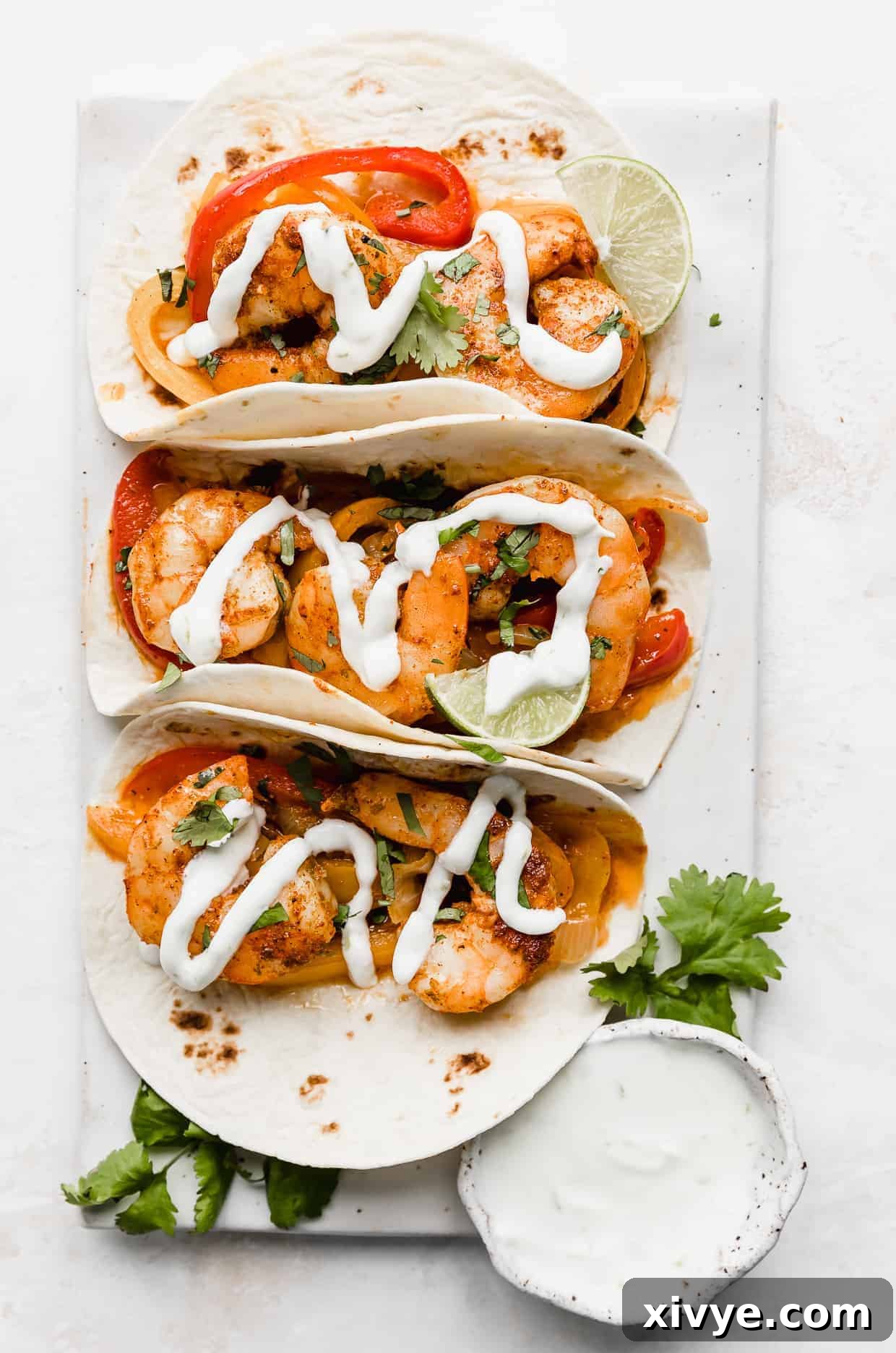 Sheet Pan Fiesta Shrimp 2 Overhead photo of three perfectly assembled shrimp fajitas on a white background, garnished with fresh cilantro and a delicate drizzle of homemade lime crema.