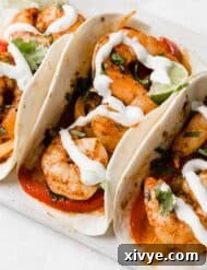 Sheet Pan Fiesta Shrimp 9 Sheet Pan Shrimp Fajitas drizzled with white Lime Crema on a white plate and white background.